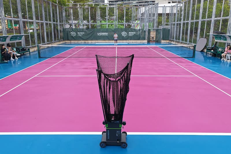 Tennis ball machine set up at the baseline on a bright outdoor tennis court