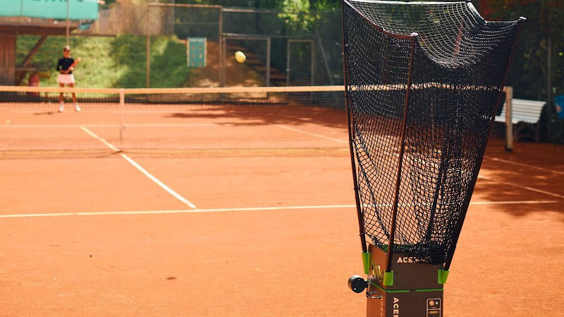 Acemate tennis ball machine feeding balls during practice on an outdoor clay court